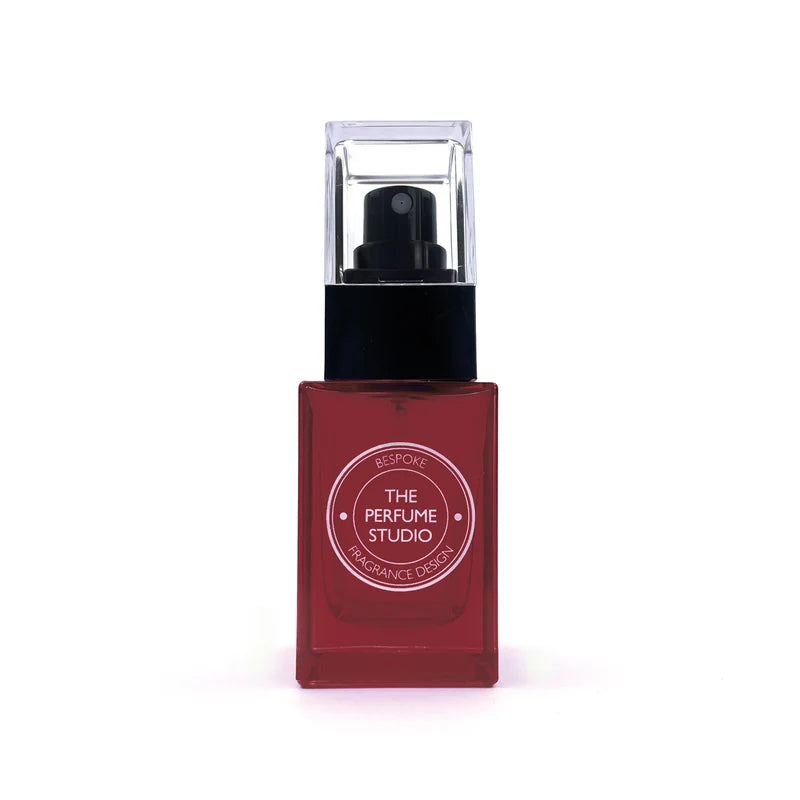 A square-shaped red perfume bottle with a black pump and a clear protective cap, featuring a circular white label that reads 'THE PERFUME STUDIO'.