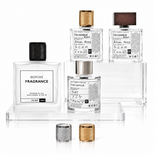 A set of clear glass fragrance bottles with various black, gold, and brown caps, displayed on clear acrylic risers against a white background.
