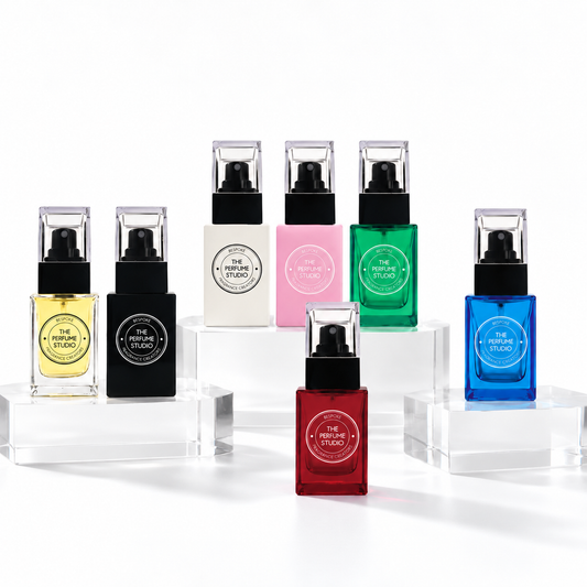 Seven square glass perfume bottles with black pump caps arranged on clear acrylic blocks against a white studio background  - designed to be refilled with bespoke fragrance.