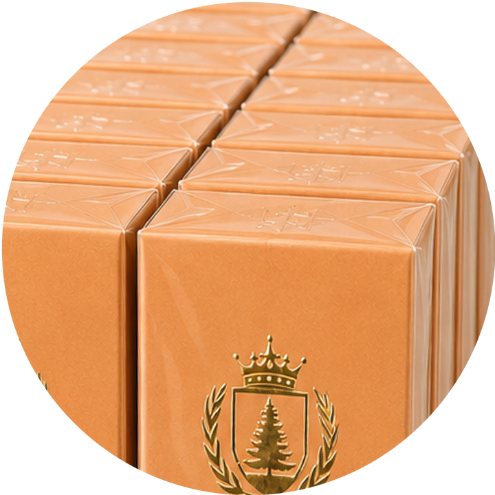 A close-up circular view of multiple peach-orange rectangular boxes stacked together, each embossed with a logo and featuring a gold crest with a crown and tree on the front box.