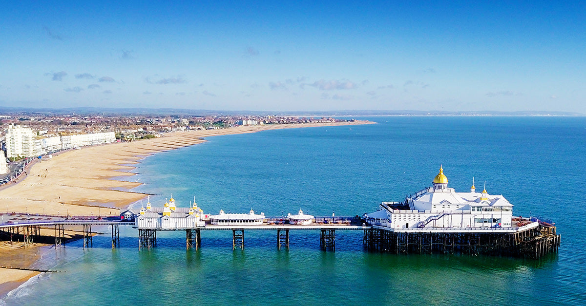 Aerial coastal view of Eastborne with the pier extending into turquoise water, sandy beach, coastline, and blue sky.