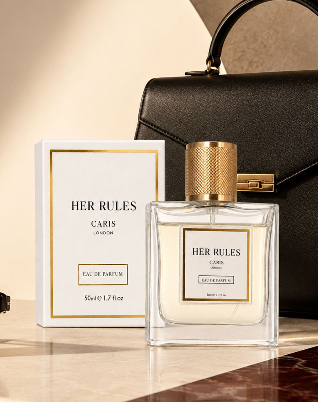 A bottle of Her Rules Caris London Eau de Parfum with a gold cap stands next to its white and gold box, styled in front of a black leather handbag on a polished marble surface.