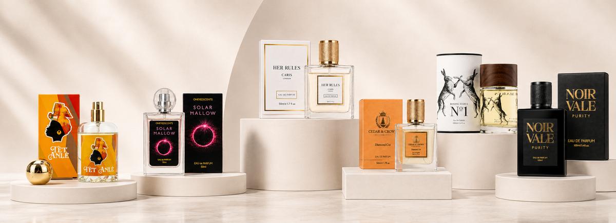 A curated collection of luxury fragrance products from Her Rules to Noir Vale displayed on white cylindrical pedestals against a warm beige background with soft diagonal shadows.